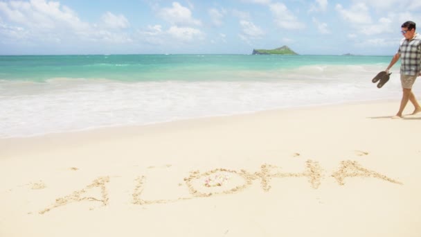 ワイマナロビーチ オアフ島 2023年8月 トロピカルビーチで砂で書かれたアロハの言葉で歩くハッピーカップル Alohaは エキゾチックなハワイの島に関するメッセージを歓迎します パラダイス サマー バケーション — ストック動画