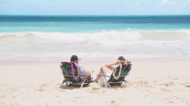 奢华的热带度假胜地的生活方式背景 两名游客坐在海滩椅子上休息 男人和女人享受蓝色海洋的倒影 美国夏威夷暑假期间游客们在海滩晒日光浴 — 图库视频影像