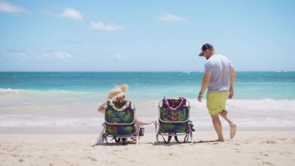 リゾートライフスタイルの背景 男はビーチチェアでリラックスするために女性に参加します バックビューのカップルは青い夏休みを楽しんでいます 青い海のビーチで太陽浴をする旅行者 豪華な熱帯ホリデー ハワイ アメリカ — ストック動画
