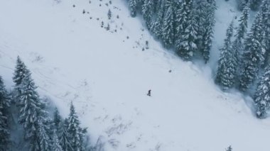 Washington kış tatili gezisi. Kış sporları arka planı. Kar fırtınasında tepelerden kayakçıların üstünde yavaş çekim yapan drone. Stevens Geçidi 'ndeki sinematik kış dağ ormanı.