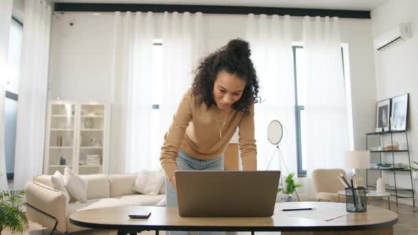 从家里远程工作的有色女人 快乐忙碌的多民族企业家站在现代客厅的工作甲板上 背景是动态的 笑着在笔记本电脑上工作的分娩妇女 — 图库视频影像