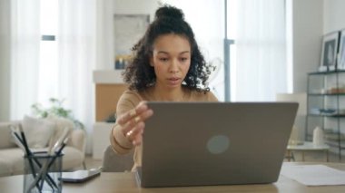 Yeni iş günü konseptine yeni bir başlangıç. Genç bir kadın online takım projesine başlamak için dizüstü bilgisayar açıyor. Uzaktan çalışma konsepti. Modern odada kıvırcık etnik kadın girişimci