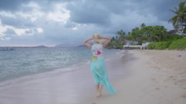 Hawaii Adası 'ndaki tropik cennete gidip arka planı kopyalayın. Gün batımından sonra egzotik sahilde yürüyen genç bir kadını takip eden kamera. Mavi plajlı turist hasır şapka ve giyip sinematik doğanın tadını çıkarıyor.