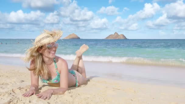 幸せな顔の若い女性は砂浜で日焼けする オアフのビーチに横たわり 夜の太陽を楽しんでいる揚げたわら帽子の笑顔の観光客 ランカイビーチで女性旅行者の日光浴 モッカイ諸島ビュー — ストック動画
