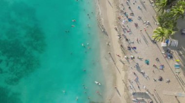 Zengin turistler açık havada renkli plaj şemsiyelerinin altında dinleniyorlar. Tropik tatil beldesi yaşam tarzı Oahu. Mavi okyanusta yüzen erkek ve kadınların genel manzarası. Gezginler yaz tatilinde güneşleniyor