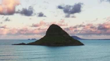 Çinlilerin Şapka Piramit Adası silueti sinema arka planında pembe renkli bulutlar. Kualoa Çiftliği 4K yakınlarındaki Kaneohe Körfezi 'ndeki Mokolii bazalt adası. Oahu adasındaki ünlü Hawaii simgesinin manzarası