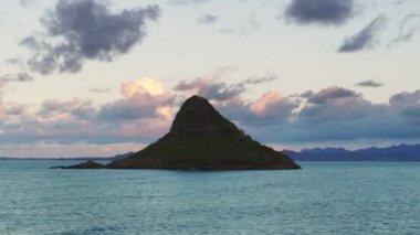 Kualoa Çiftliği 4K yakınlarındaki Kaneohe Körfezi 'ndeki Mokolii bazalt adası. Oahu adasındaki ünlü Hawaii simgesinin manzarası. Çinlilerin Şapka Piramit Adası silueti sinema arka planında pembe renkli bulutlar