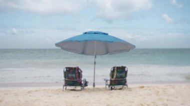 Renkli plaj sandalyeleri ve mavi okyanusun yanında güneş şemsiyesi. Yaz tatili ve turizm için tatil konsepti. İlham verici tropikal manzara 4K. Güzel sahil Waimanalo, Oahu Adası, Hawaii ABD