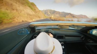 Cabriolet 'teki egzotik Hawaii adasını çatısız gezen mutlu gezgin. Açık hava macerası yaz tatili. Üstü açık modern araba arka koltukları manzaralı okyanus kıyısından geçen şık bir genç kadın.