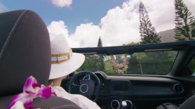 Cabriolet 'te egzotik Hawaii' yi çatısı olmadan keşfeden şık bir gezgin. Açık hava macera yaz gezisi. Üstü açık modern araba arka koltukları, Hindistan cevizi palmiyeleriyle tropikal adanın yanından geçen şık bir kadına bakıyor.