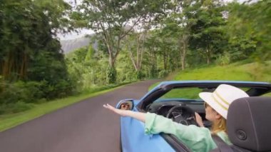 Şık bir turist, kiralık arabasından çatısı olmadan elini uzatıyor. Hawaii gezisinde botanik bahçesinde araba kullanan bir kadın. Elleri açık, üstü açık arabalarla gezen, rüzgar estiren özgür kız.