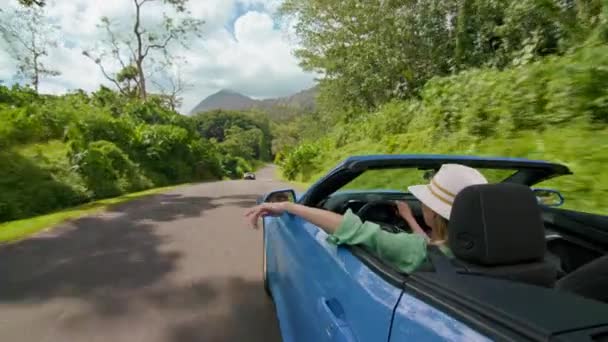 ハワイ旅行で植物性熱帯ガーデンを運転する女性 コンバーチブルカーの手から手を引いた無料の女の子は 顔に風が吹く スタイリッシュな観光客は屋根なしでレンタカーから手を伸ばします — ストック動画