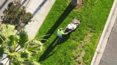 Calabasas, Los Angeles 'taki The Commons alışveriş merkezinde çim biçme makinesiyle çim biçen erkek işçiyi çekiyoruz. Üniformalı bir adam sokakta çim biçme makinesi kullanıyor, 4K görüntü.