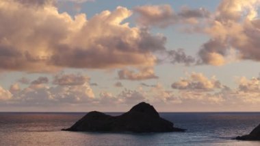 Hawaii adalarında dramatik manzara. Oahu turizm kavramı. Renkli gündoğumunda rüzgârlı kıyılarda iki küçük ada. Na Mokulua adalarının siluetleri okyanusta, parlak bulutların altında.