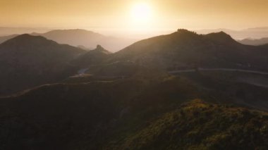 Malibu 'daki Kanan yolunun günbatımında Kaliforniya, ABD' deki panoramik görüntüleri. Virajlı otoyolda uçan İHA ve gün doğumunda dağın tepesindeki Malibu Rocky Oaks Estate Vineyard 'da 4k' lik görüntüler.