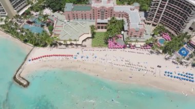 Sihirli Waikiki sahilinde pahalı, pembe bir tatil köyü. Hawaii 'deki Oahu Adası ikonik oteli. Kumsalın keyfini çıkaran insanların üstündeki havadan. Okyanus manzaralı Hawaii pembe otel binası