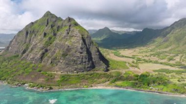 Güneşli yaz gününde Kualoa Vadisi manzarası. Destansı hava yolculuğu arka planı 4K Hawaii adası. Yüksek sarp yeşil dağ manzaralı uzak adalara açık hava macerası. Nefes kesici mavi okyanus manzaralı ABD