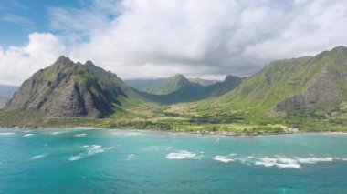 Nefes kesici mavi okyanus manzaralı ABD. Güneşli yaz gününde Kualoa Vadisi manzarası. Destansı hava yolculuğu arka planı 4K Hawaii adası. Yüksek sarp yeşil dağ manzaralı uzak adalara açık hava macerası