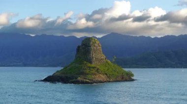 Bulutlu gökyüzünün arka planında Mokolii bazalt adası. Hawaii 'deki Oahu Adası manzarası. Çinlilerin sınırında hindistan cevizi palmiyesi ağaçları Kualoa Ranch dağının arka planında Şapka Adası