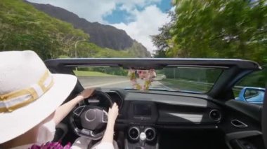 Kadın Oahu Adası 4K 'dan geçiyor. H3 otobanından geçen mavi üstü açık arabalı mutlu turist. Cabriolet 'in açık arabasından görülen manzara Hawaii manzarası. Çiçekli zarif kadın destansı manzaranın tadını çıkarıyor.