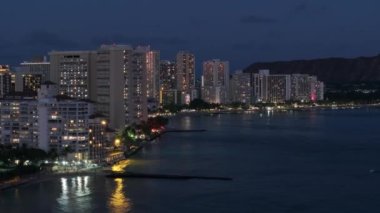 Hava karardıktan sonra Hawaii 'nin en büyük şehrinden insansız hava aracı vuruldu. Şehir merkezinde, tropik ada Oahu 4K 'da. Gece Waikiki sahilinin manzarası. Güzel Honolulu modern binaları gece aydınlandı.