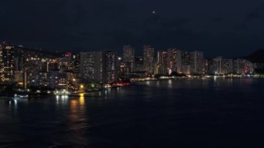 Waikiki sahilindeki tatil köylerinde. Geceleri aydınlatılmış güzel Honolulu modern binaları. Hava karardıktan sonra Hawaii 'nin en büyük şehrinden insansız hava aracı vuruldu. Şehir merkezindeki tropik ada Oahu 4K turizmi