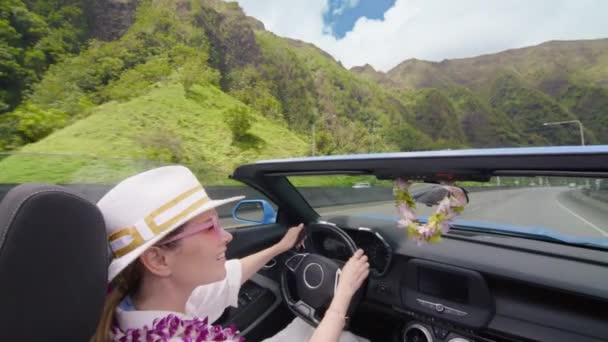 カブリオレのオープンカーから見た景色のハワイ 壮大な景色を楽しむレイの花に優雅な女性 女性はオアフ島4Kで旅行します H3ハイウェイUsaで運転するブルーコンバーチブルカーでハッピーな観光客 — ストック動画