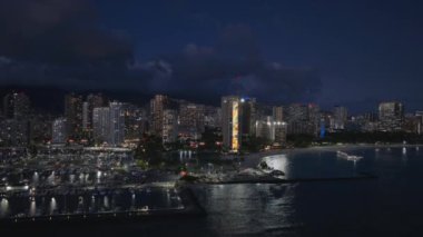 Gece Waikiki sahilinin manzarası. Geceleri aydınlatılmış güzel Honolulu modern binaları. Hava karardıktan sonra Hawaii 'nin en büyük şehrinden insansız hava aracı vuruldu. Şehir merkezindeki tropik ada Oahu 4K