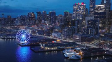 Seattle şehir merkezindeki deniz manzarası ve finans bölgesi gökdelenleri ve binaları karanlık kış gecesinde. Şehir manzarasının 4K b-roll drone görüntüsü. Aydınlatılmış gece şehri ABD