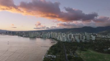 Oahu adasındaki Honolulu şehrinin üzerinde güzel bir yaz günbatımı. Waikiki tatil köyleri ile şehir merkezindeki modern şehrin hava manzarası. Kapiolani Bölgesel Parkı, altın gün doğumunda. Hawaii adası manzarası 4K