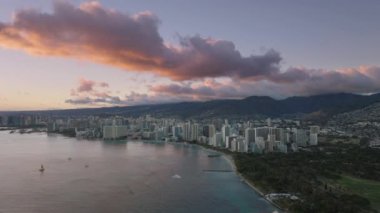 Waikiki tatil köyleri ile şehir merkezindeki modern şehrin hava manzarası. Oahu adasındaki Honolulu şehrinin üzerinde güzel bir yaz günbatımı. Altın gün batımında Kapiolani Bölge Parkı. Hawaii adası manzarası 4K