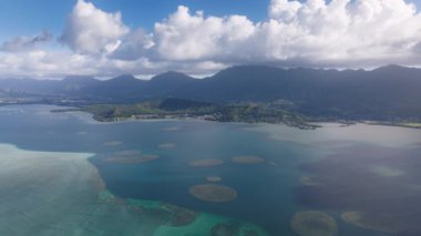 Oahu Adası seyahat geçmişi. Kaneohe Körfezi 'nde açık deniz mavisi. Havai Dağı 'nın beyaz bulutlardaki tepeleri. Hawaii turizmi 4K İHA yaz günü Kaneohe Sandbar üzerinde mavi gökyüzüyle uçuyor.