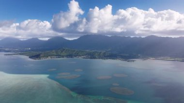 Havai Dağı 'nın beyaz bulutlardaki tepeleri. Hawaii turizmi 4K İHA 'sı yaz günü Kaneohe Sandbar üzerinde mavi gökyüzüyle uçuyor. Oahu Adası seyahat geçmişi. Kaneohe Körfezi 'nde açık deniz mavisi.