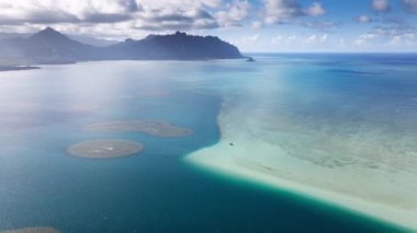 Oahu adası yolculuğu. Kaneohe Körfezi 'nde açık deniz mavisi. Kualoa dağlarının güzel silueti mavi gökyüzündeki beyaz bulutların altında. Hawaii turizmi 4K. İnsansız hava aracı yaz günü Kaneohe Sandbar üzerinde uçuyor.