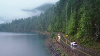 Sinematik ve yeşil orman olimpiyat ulusal parkı. Washington yağmur ormanlarındaki gezginler. Yolculuk konsepti havadan. Yağmurlu bir günde güzel bir göl boyunca turistlerle dolu arazi aracı manzaralı bir yoldan geçiyor.