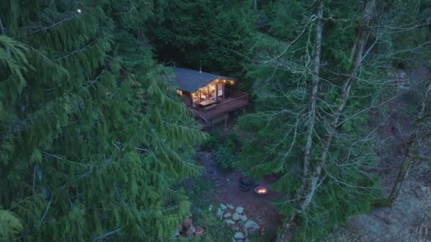 小木屋隐藏在山林常绿树之间 晚上在森林中间的小木屋里神奇的华盛顿森林中的木制小木屋 有燃烧火坑的乡村住宅 — 图库视频影像