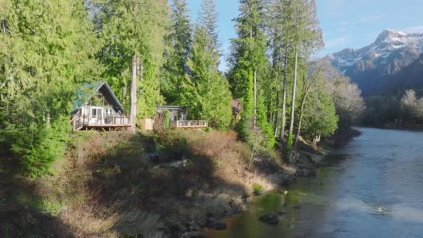 阳光明媚的时候在树林里的小木屋里 森林小屋在神奇的华盛顿森林河流与山景 蓝色河流4K山林常绿树之间的乡村小屋 — 图库视频影像