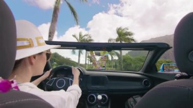 Üstü açık modern araba arka koltukları, Hindistan cevizi palmiyeli tropikal adanın yanından geçen şık bir kadına bakıyor. Cabriolet 'te egzotik Hawaii' yi keşfeden mutlu bir gezgin.