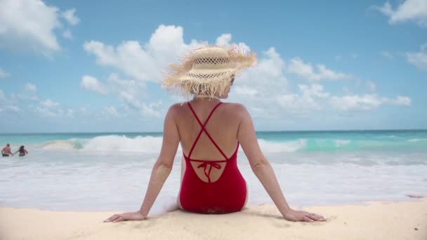 シネマティックなビーチバケーションの背景 人々は夏に美しいティールブルーの海とパラダイス島に旅行します 観光コンセプトのスローモーション 赤い水着とわら帽子のバックビュー女性は海4Kを楽しむ — ストック動画