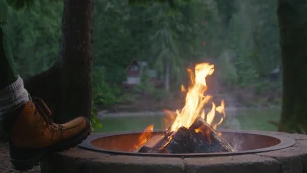 緑のスプルースの森で明るい燃える炎を楽しんでいる女性 ネイチャーキャンプ4K 火のピットに木製のログを置く女性の手のクローズアップショット 週末休暇中の屋外キャンプアドベンチャー — ストック動画