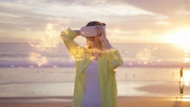 海のビーチで屋外に立っている未来拡張現実ソフトウェア インターフェイスを使用して魅力的な若い女性 風光明媚な夕日で未来的なプロジェクトでVfxアニメーションを見るためにヘッドセットを着ている女性 — ストック動画