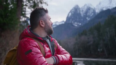 Turist sırt çantalı orta yaşlı bir adamın dağlarda yürüyüş yaparken portresi. Arka plandaki kayalık dağ zirvelerinde uzak doğa beldelerindeki gezgin turist. Erkek gezgin açık hava bulutlu gününde ormanı keşfediyor.