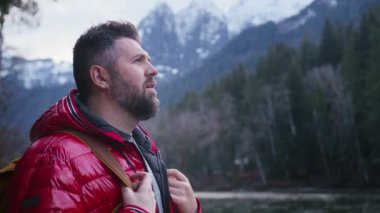 Erkek gezgin açık hava bulutlu gününü keşfediyor. Arka plandaki kayalık dağ zirvelerinde uzak doğa beldelerindeki gezgin turist. Turist sırt çantalı orta yaşlı bir adamın dağlarda yürüyüş yaparken portresi.