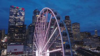 Waterfront Park rıhtımındaki lunaparkta Seattle Büyük Tekerlek 'in renkli aydınlanması. Geceleri Seattle 'ın panoramalı sineması. Şehir merkezindeki güzel gökdelenler. ABD turizmi.