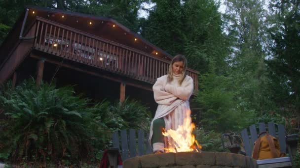 在背景下的绿云杉森林里 女性在篝火边热身 游客们在舒适的毛毯里取暖 周末在森林小木屋里燃着篝火 放松的女人享受着篝火的乐趣 — 图库视频影像
