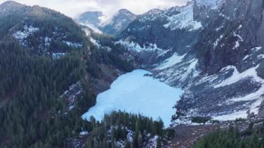 Soğuk kış gününde Washington dağ ormanı manzaralı hava. Yüksek dağ sırtına gizlenmiş güzel donmuş dağ gölü. Küçük dağ gölünün tepesinde mavi buzlu sinematik doğa havası