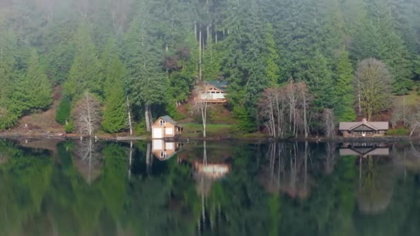 电影中的空中高山湖景 一面镜子中倒映在水面上的常绿森林的和平景致 低雾云雾中山林景观中的滨水木小屋 — 图库视频影像