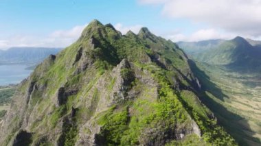 Oahu seyahat arka planı USA 4K. Güneşli yaz gününde destansı dağ zirveleri. İnsansız hava aracı dağ sırtı boyunca manzaralı zirvelerle uçuyor. Yeşillik arka planı yemyeşil. Hawaii Doğa Güzelliği Kualoa Parkı