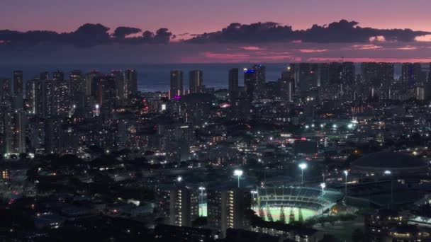 ワイキキリゾートの上に紫色の雲が広がる風光明媚なピンクの夕日空 ホノルルのダウンタウンにある近代的な建物のシネマティックな街並み 太平洋のハワイ州オアフ島の夜の都市を巡る空中ビュー — ストック動画