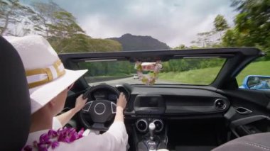 Yaz tatilinde Cabriolet araba kullanan Orkide Lei ve beyaz şapkalı bir kadın. Sinematik yeşil dağlarla Oahu adasını keşfeden mutlu gezgin. Kız kendini özgür hissediyor. Arka koltuktan üstü açılır arabayı izle